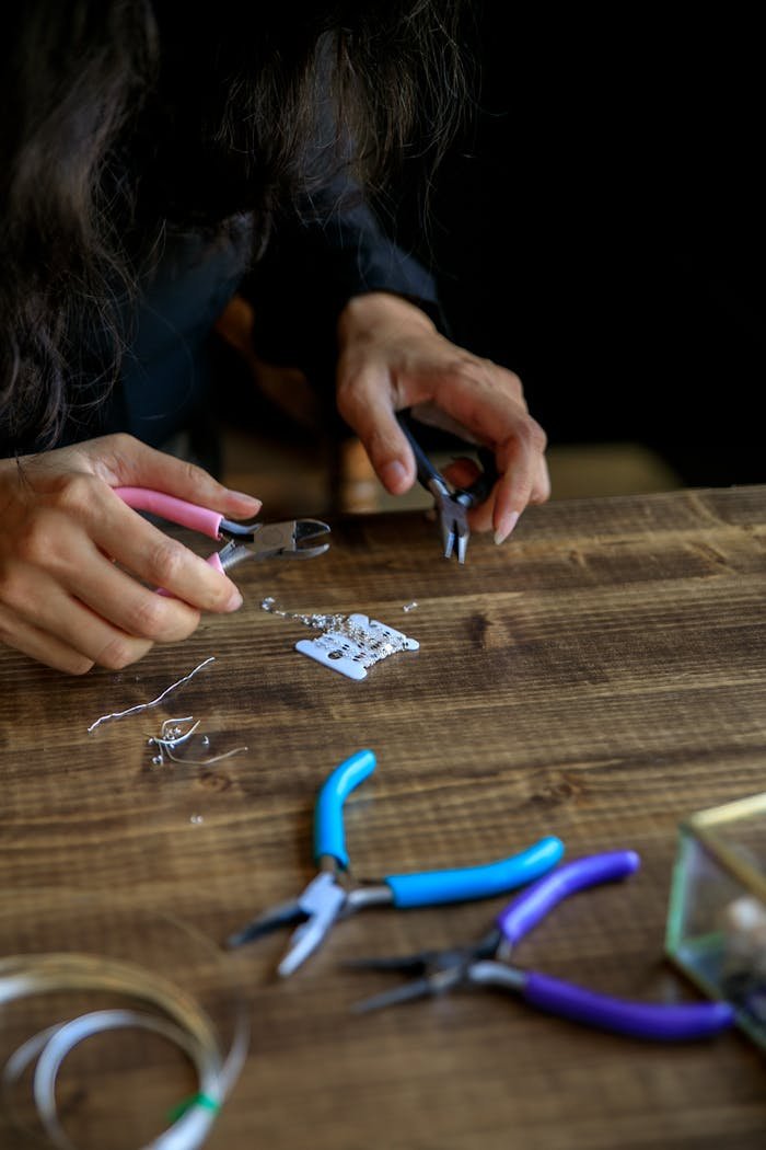 Close-up of a woman making jewelry with pliers and beads on a wooden table.