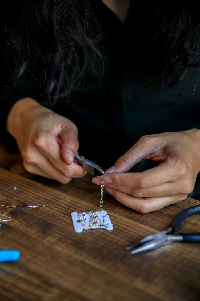 Focused shot of handmade jewelry making with pliers and beads on a wooden table.