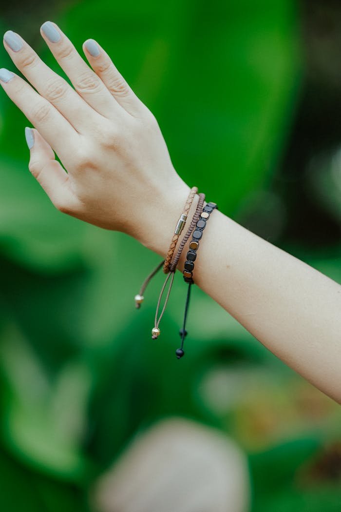Close-up of a woman's hand wearing bracelets against lush green background.