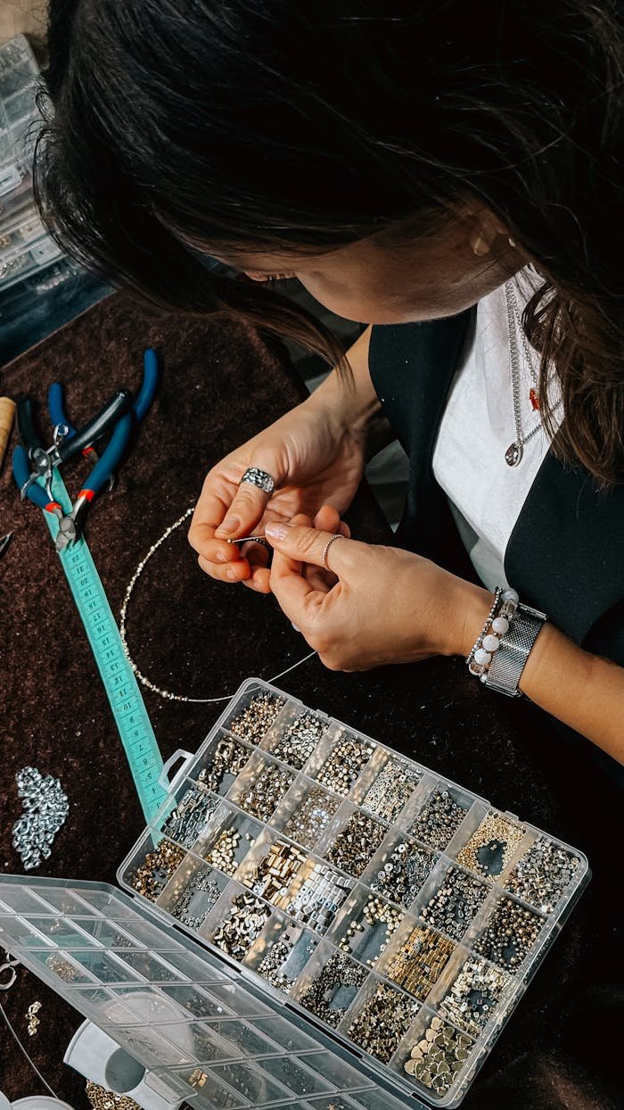 Close-up of a woman crafting jewelry with a bead organizer and tools.